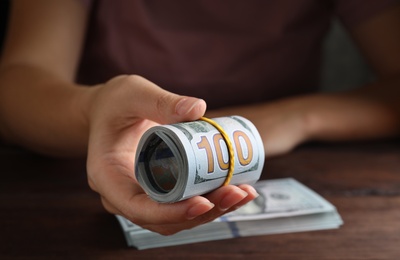 Woman holding rolled dollar banknotes at wooden table, closeup