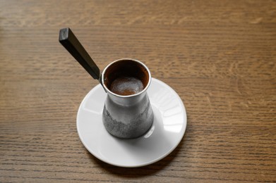 Photo of Jezve with fresh coffee on wooden table