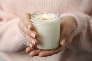 Photo of Woman holding burning candle with wooden wick, closeup