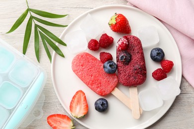 Photo of Plate of tasty berry ice pops on light wooden table, flat lay. Fruit popsicle