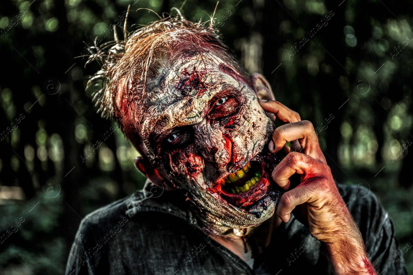 Photo of Scary zombie with bloody face outdoors, closeup. Halloween monster