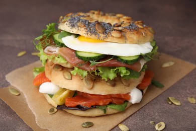 Photo of Tasty bagel with cured ham, egg, salmon and vegetables on brown table, closeup