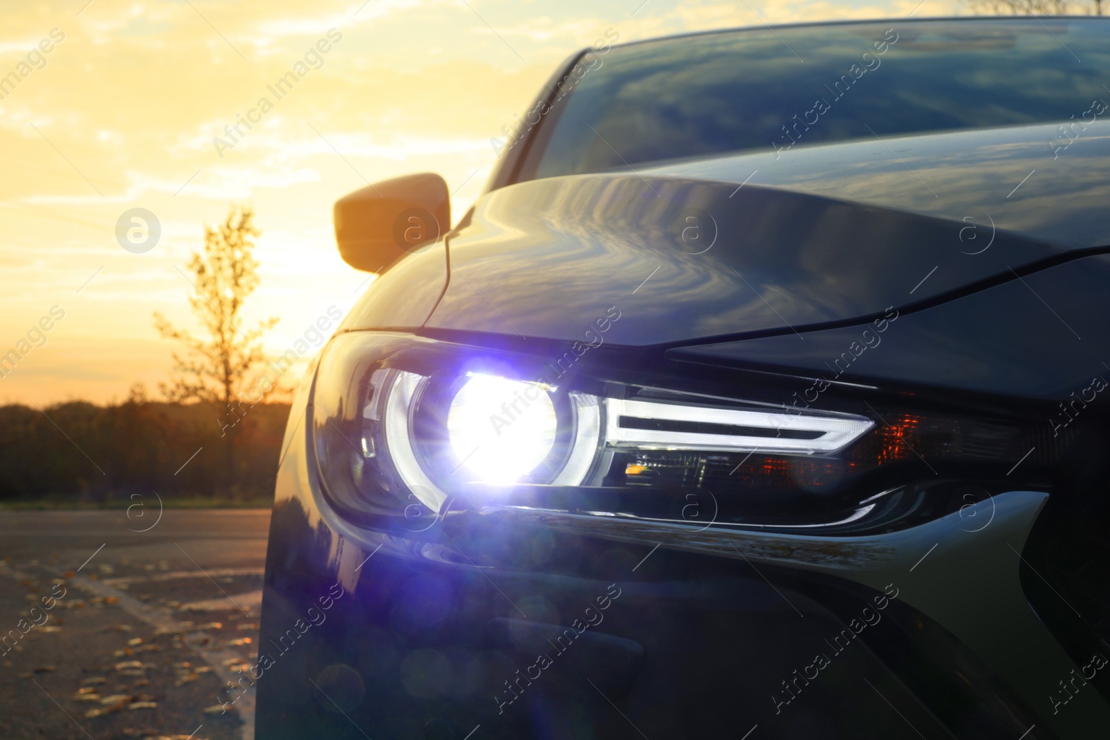 Photo of Black modern car parked on road at sunset, closeup of headlight