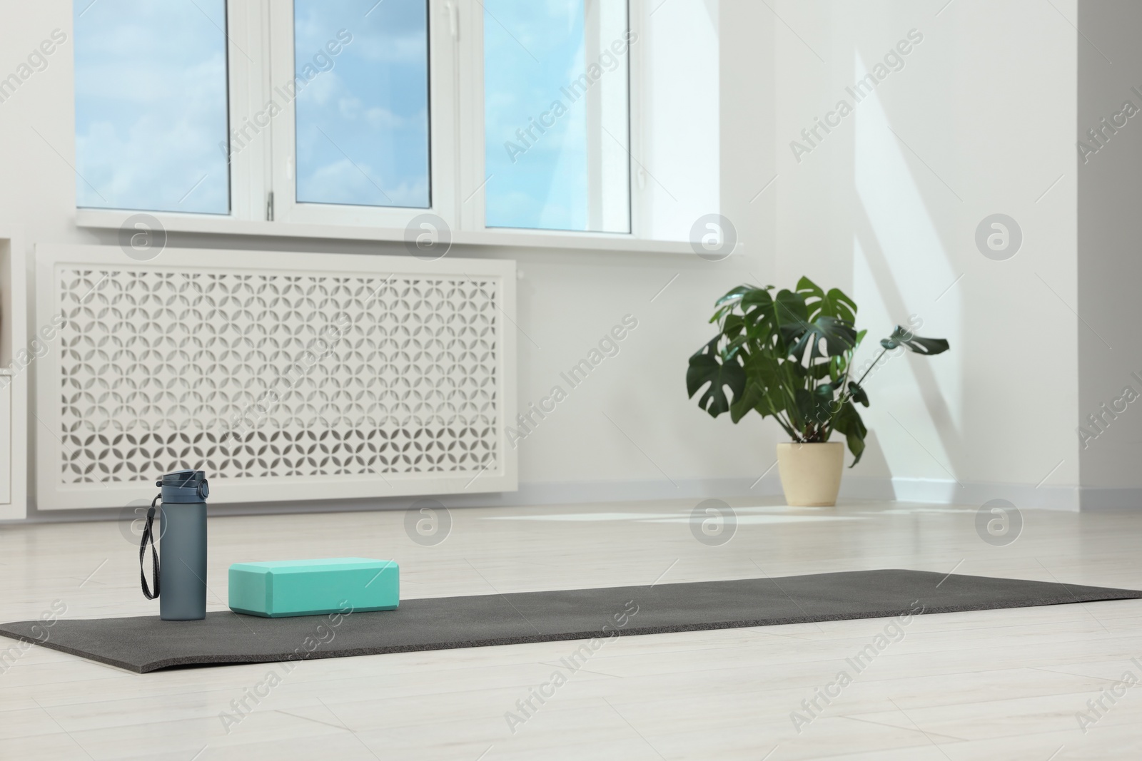 Photo of Exercise mat, yoga block and bottle of water on floor in room