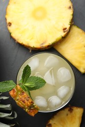 Photo of Delicious pineapple juice with fresh fruit and mint on black table, flat lay