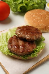 Photo of Delicious fried patties, lettuce and bun on white table. Making hamburger