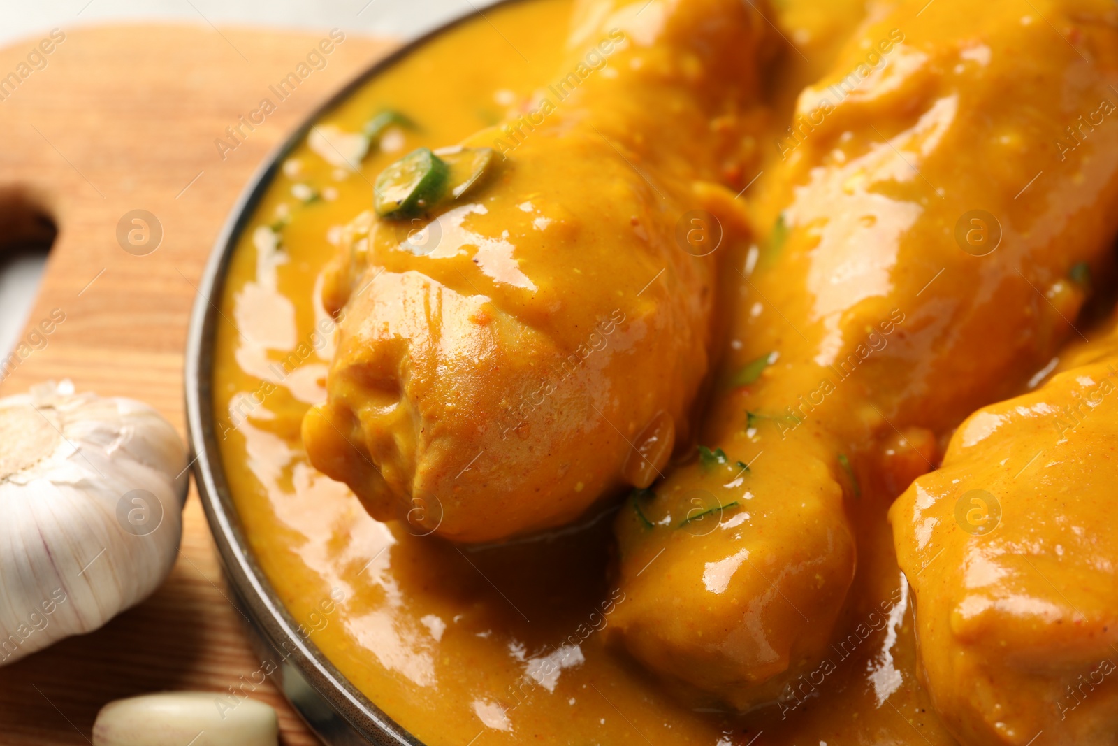 Photo of Tasty chicken curry and garlic on wooden board, closeup