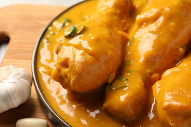 Photo of Tasty chicken curry and garlic on wooden board, closeup