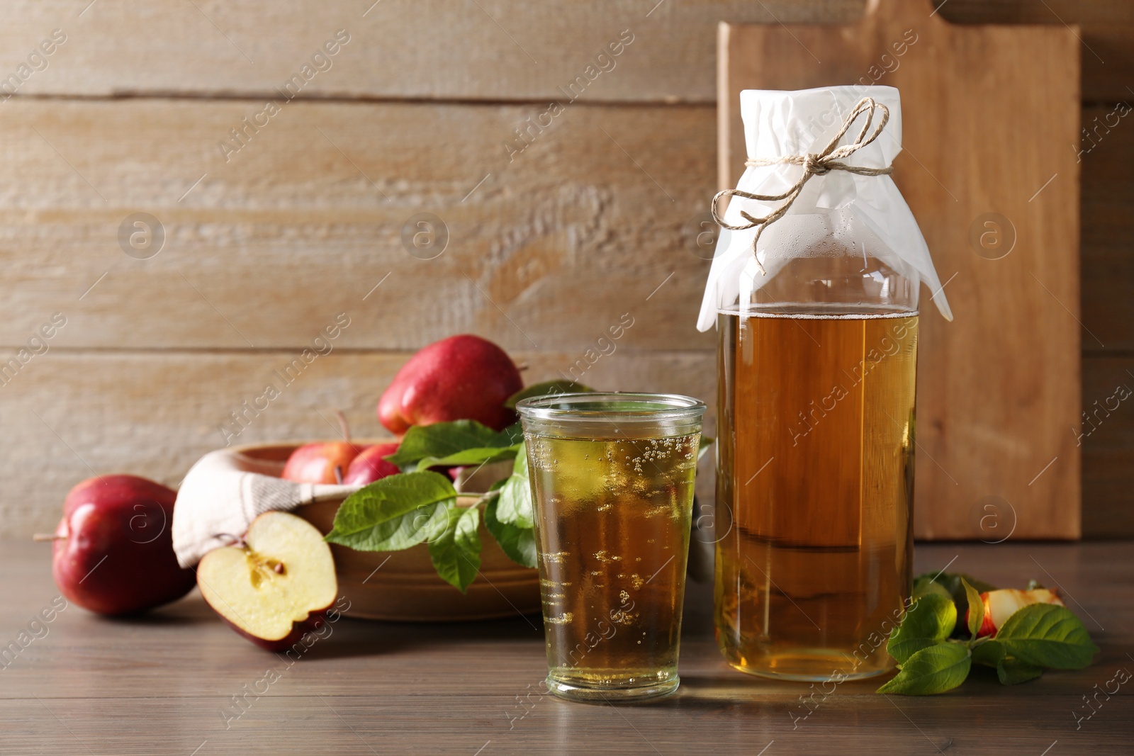 Photo of Delicious cider and apples with green leaves on wooden table, space for text