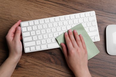 Photo of Woman wiping keyboard with paper towel at wooden table, closeup