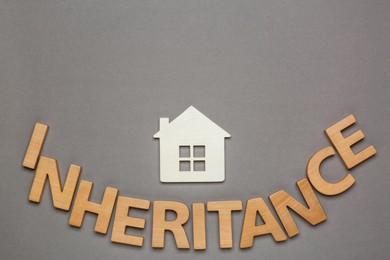 Photo of Word Inheritance made with wooden letters and house model on grey background, flat lay. Space for text