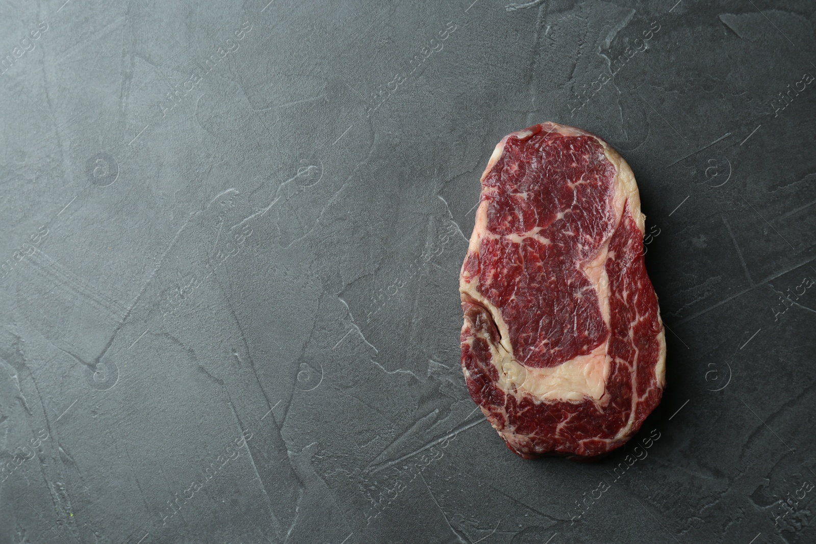 Photo of Piece of raw beef meat on grey table, top view. Space for text