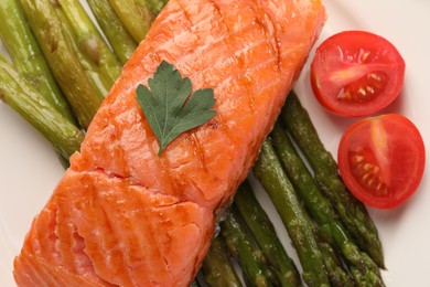 Photo of Plate with tasty grilled salmon, tomatoes and asparagus, top view