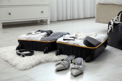 Photo of Open suitcase with clothes, shoes and accessories on floor indoors