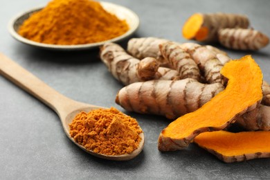 Aromatic turmeric powder and raw roots on grey table, closeup