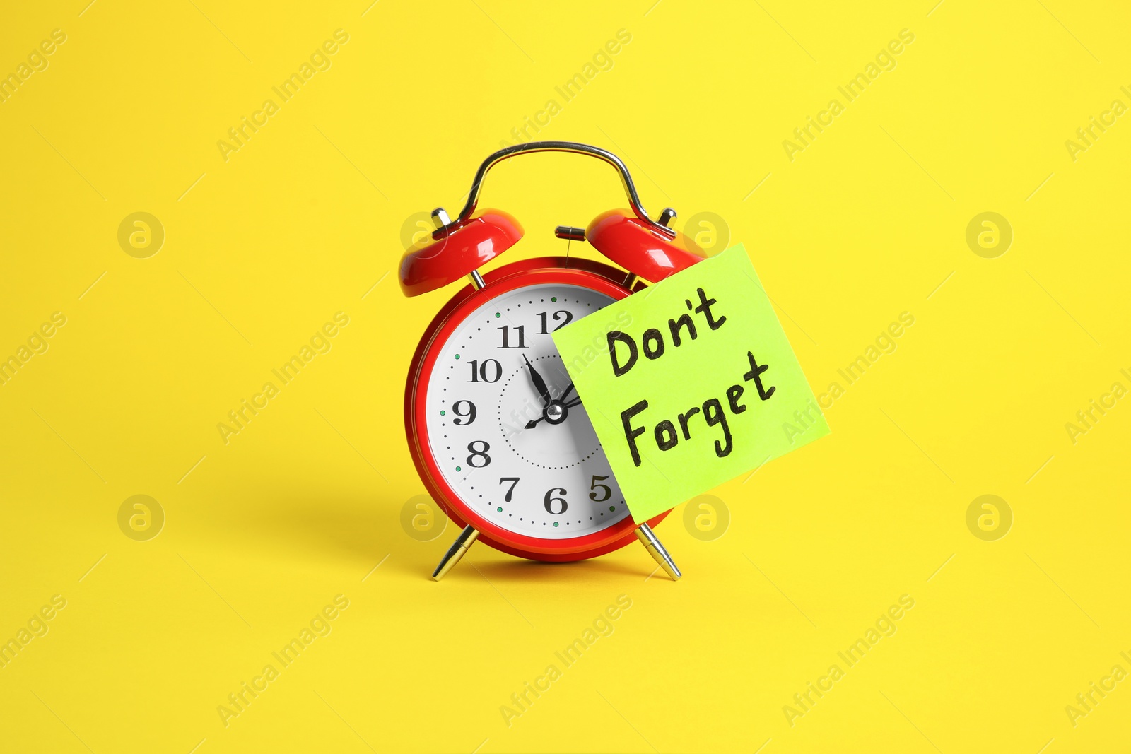 Photo of Alarm clock and reminder note with phrase Don't forget on yellow background