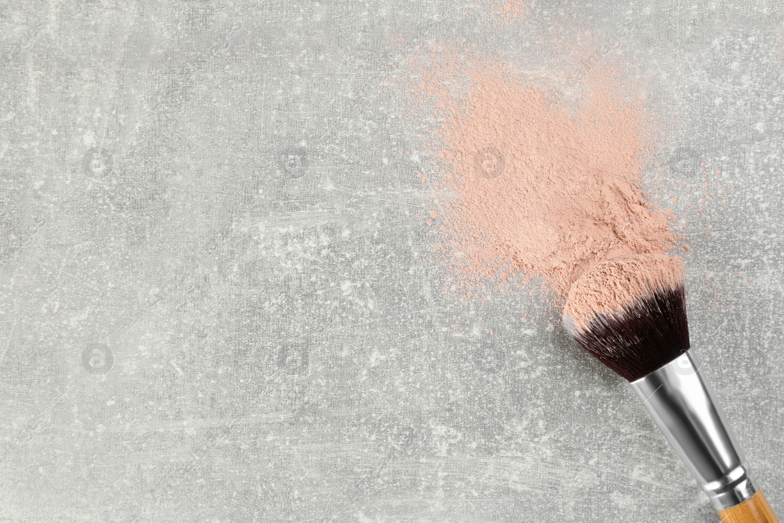 Photo of Makeup brush and scattered face powder on grey stone table, top view. Space for text