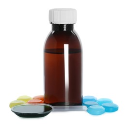 Bottle of syrup, dosing spoon and cough drops on white background