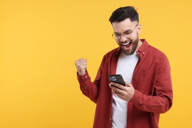 Photo of Happy young man using smartphone on yellow background, space for text