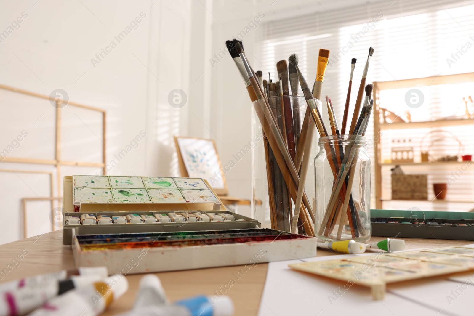 Photo of Different brushes and colorful paints on wooden table in studio. Artist's workplace