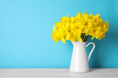 Photo of Bouquet of daffodils in jug on table against color background, space for text. Fresh spring flowers