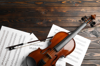 Photo of Violin, bow and note sheets on wooden table, flat lay. Space for text