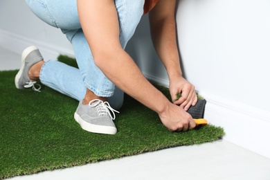 Man cutting artificial grass carpet indoors, closeup