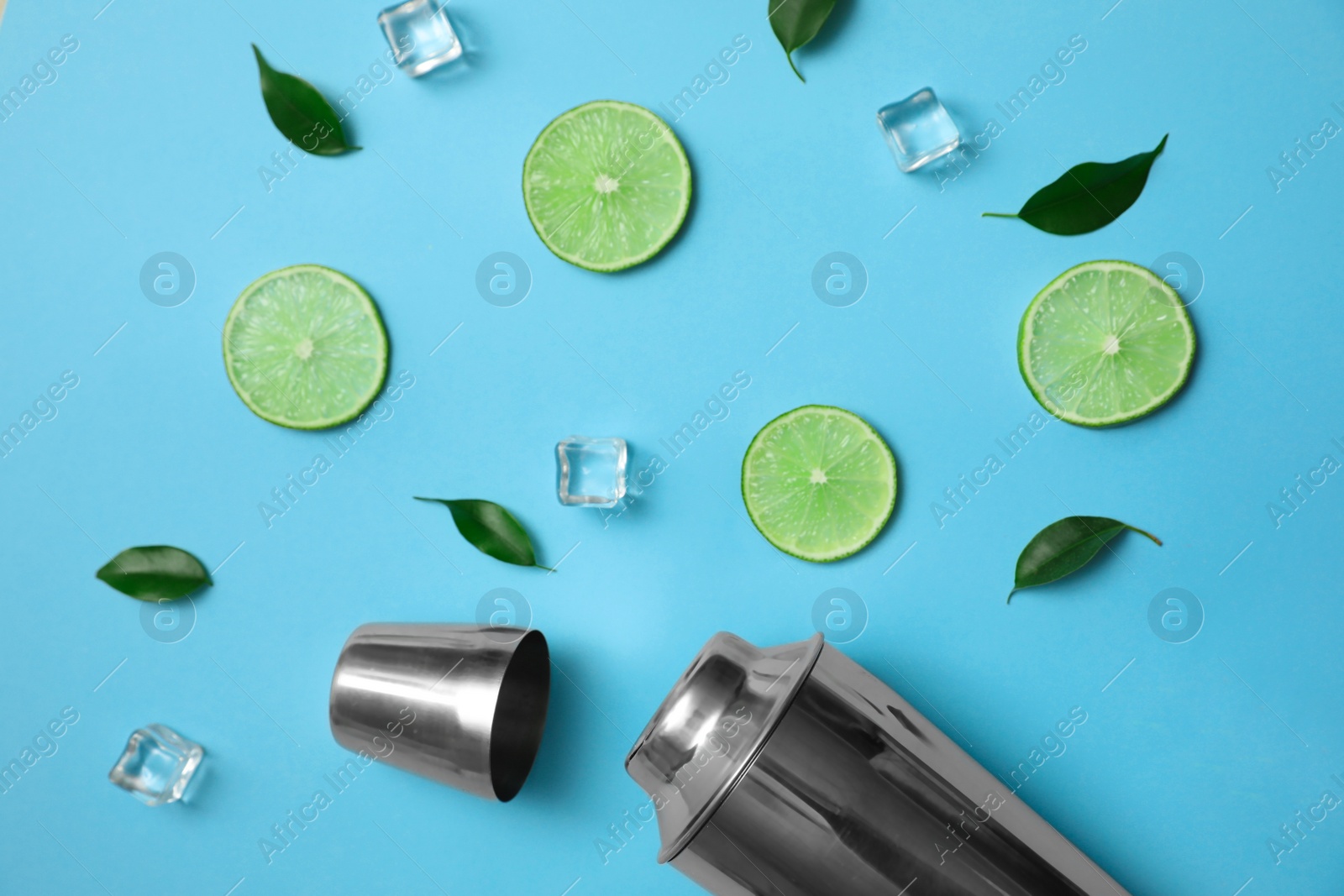 Photo of Flat lay composition with fresh juicy limes, ice cubes and cocktail shaker on light blue background