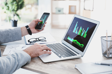 Broker working with laptop and mobile phone at table, closeup. Forex trading