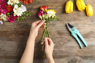 Woman making bouquet of freesia flowers at table, top view