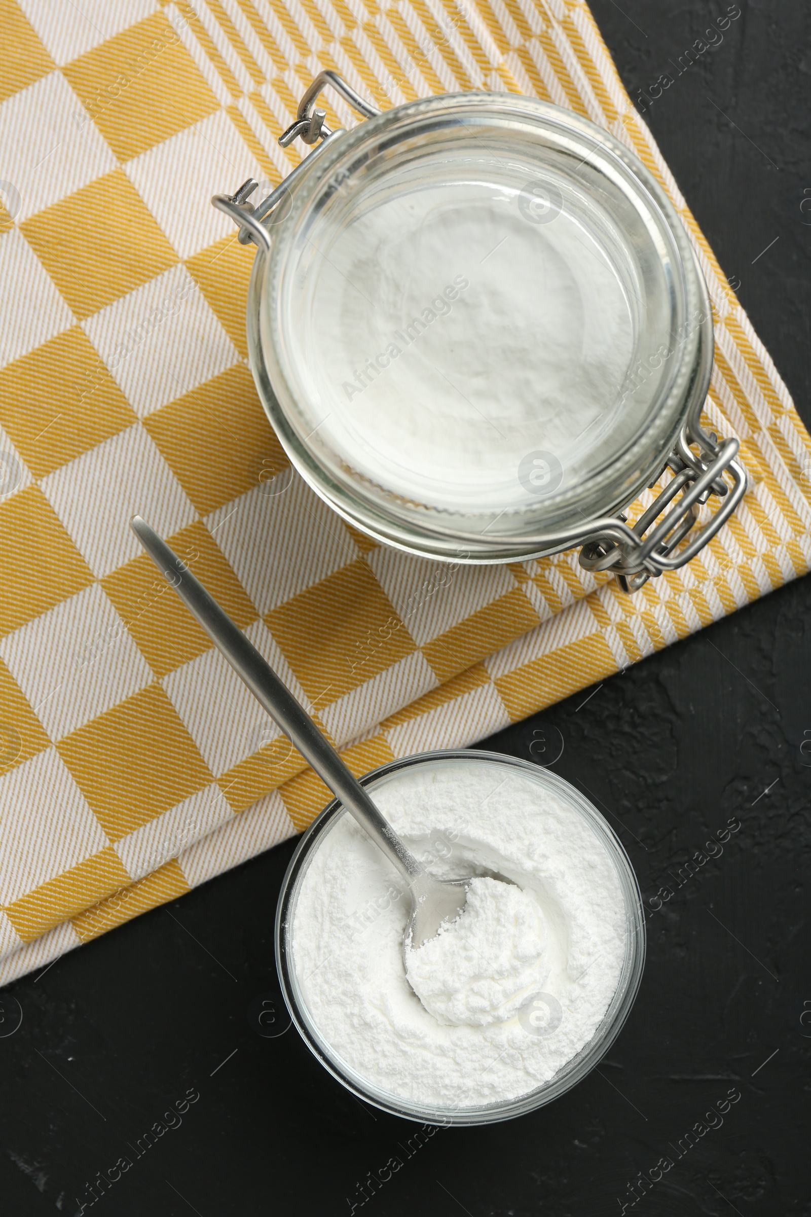 Photo of Baking powder in bowl and jar on black textured table, flat lay