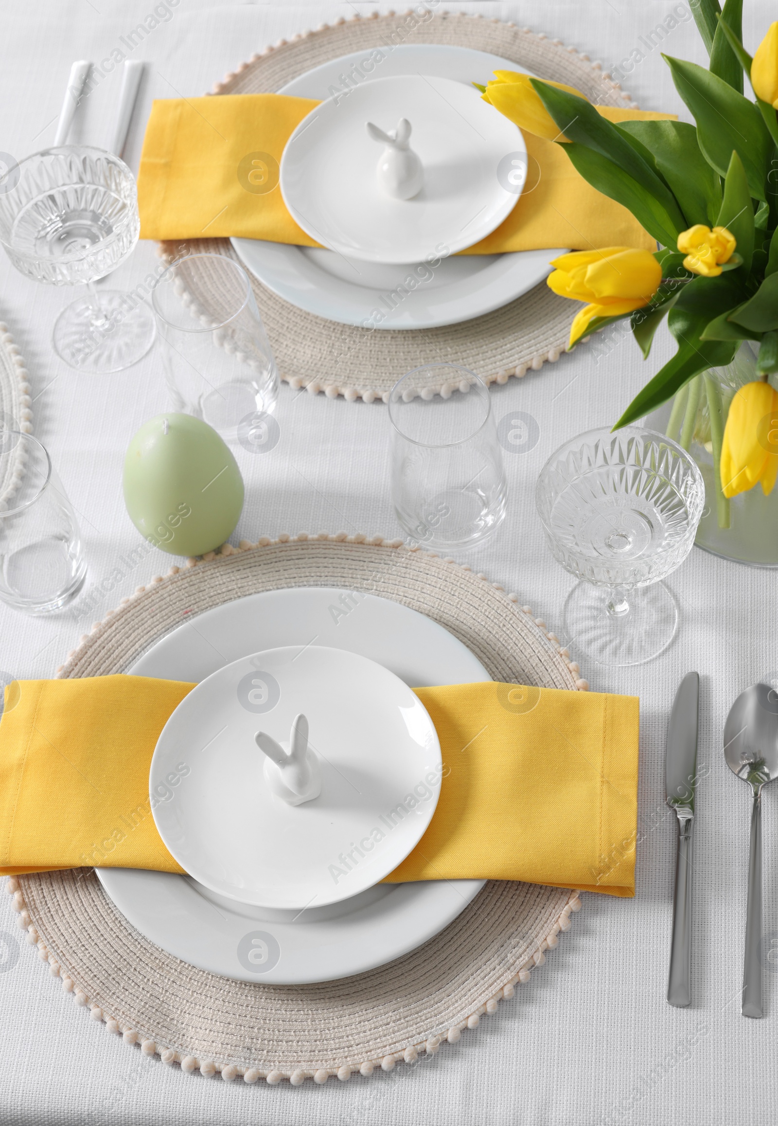 Photo of Festive table setting with glasses, plates and vase of tulips. Easter celebration