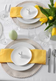 Photo of Festive table setting with glasses, plates and vase of tulips. Easter celebration