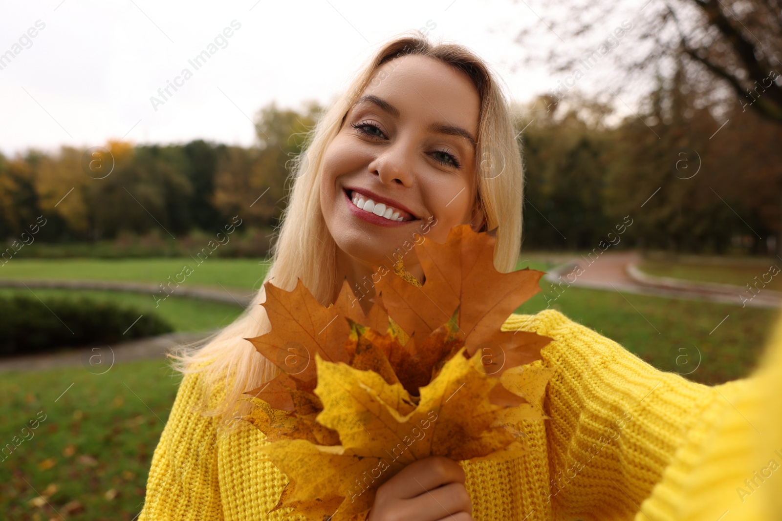 Photo of Portrait of happy woman with autumn leaves taking selfie in park