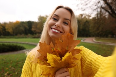 Photo of Portrait of happy woman with autumn leaves taking selfie in park