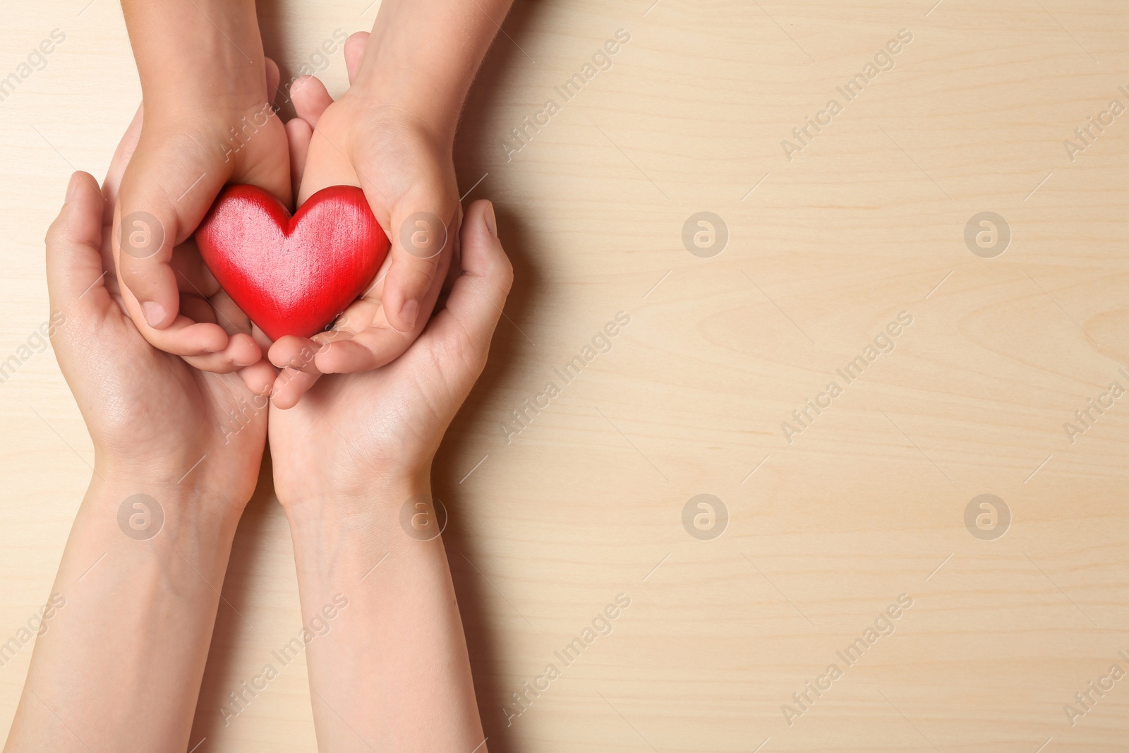 Photo of Woman and child holding heart on beige wooden background, top view with space for text. Donation concept