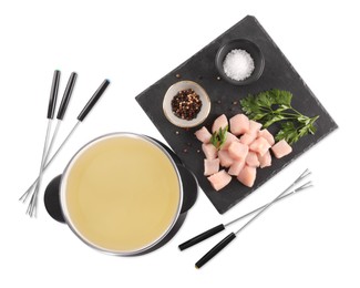 Photo of Oil in fondue pot, forks, pieces of raw meat, salt and pepper isolated on white, top view