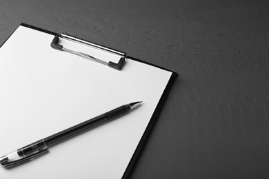 Photo of Clipboard with sheet of paper and pen on black wooden table. Space for text
