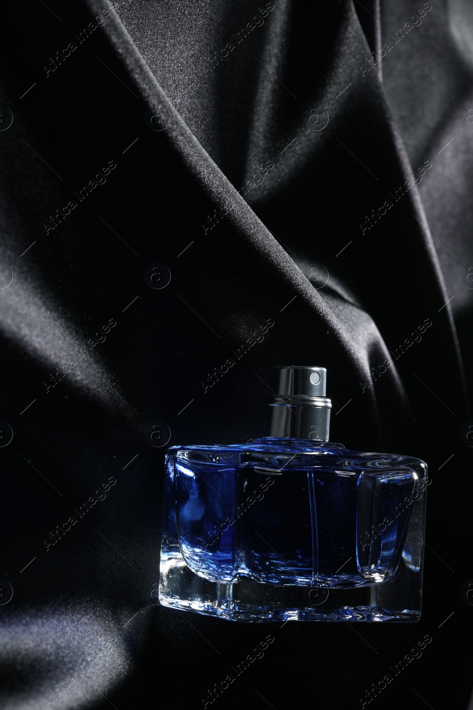 Photo of Luxury men's perfume in bottle on black satin fabric, top view. Space for text