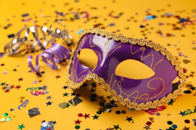 Photo of Beautiful purple carnival mask and confetti on yellow background, closeup