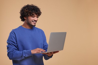 Smiling man with laptop on beige background. Space for text
