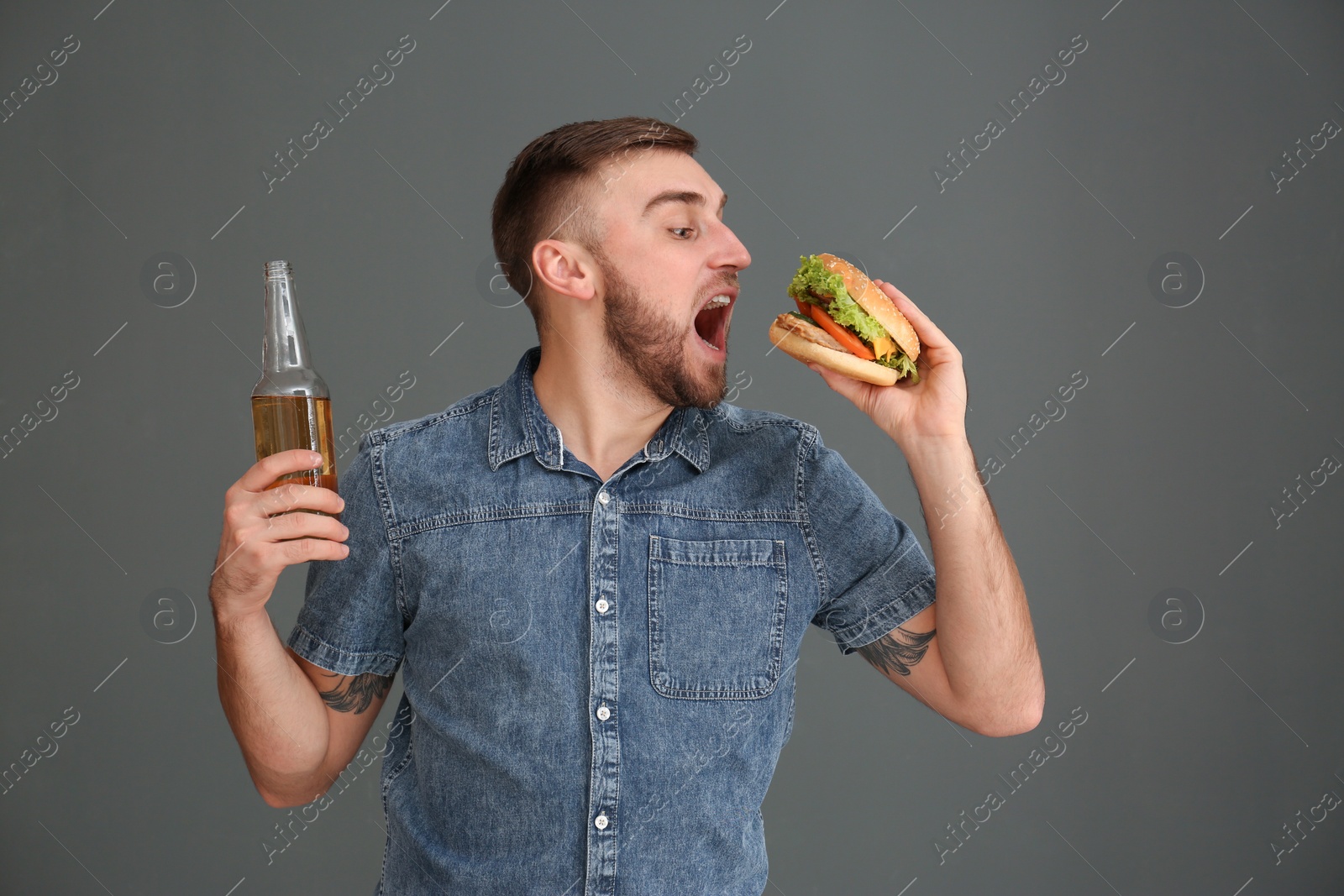 Photo of Young man with beer eating tasty burger on grey background