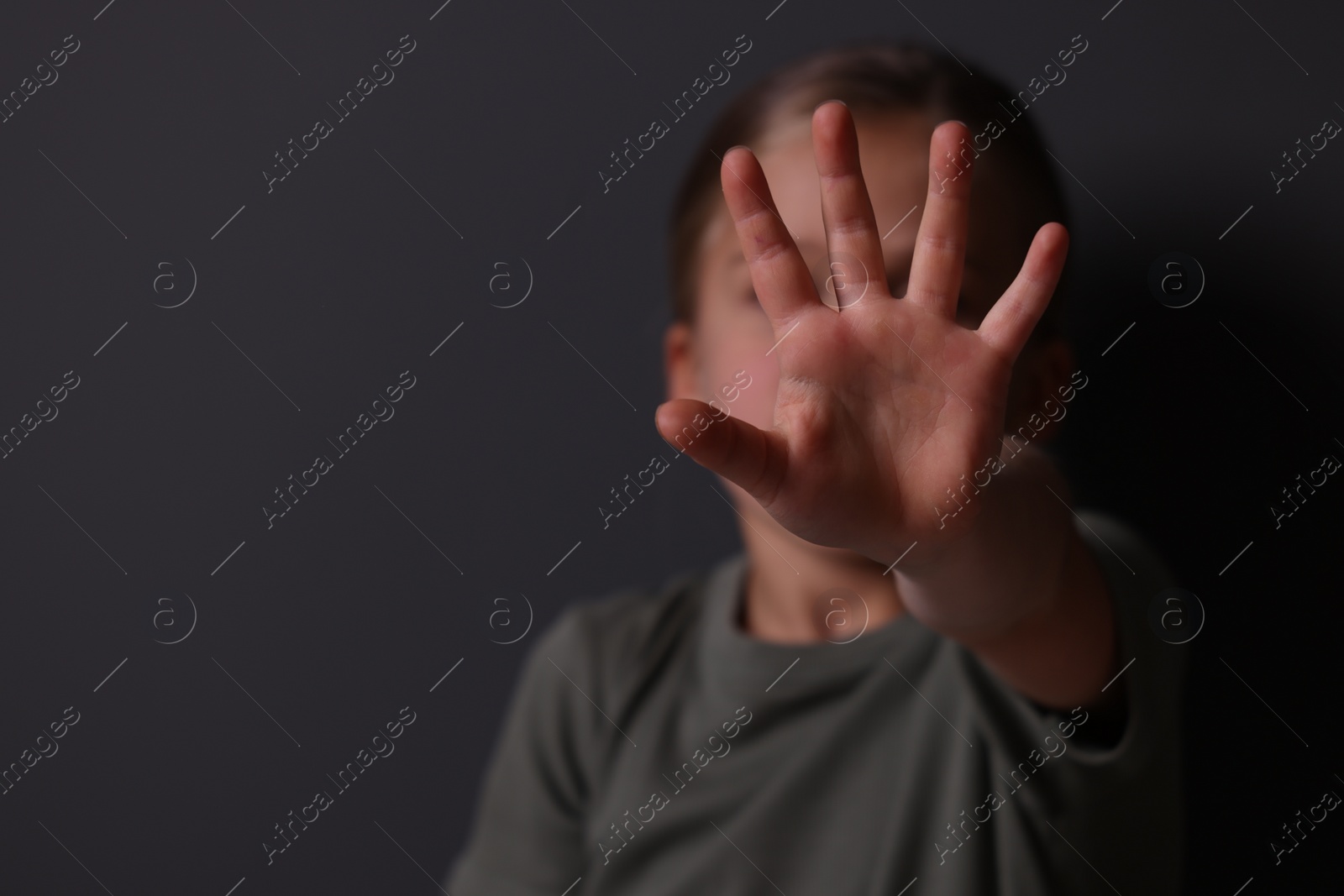 Photo of Child abuse. Girl making stop gesture near grey wall, selective focus. Space for text