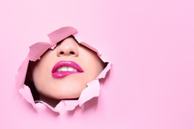 Photo of View of beautiful young woman with perfect lips makeup through hole in color paper. Space for text