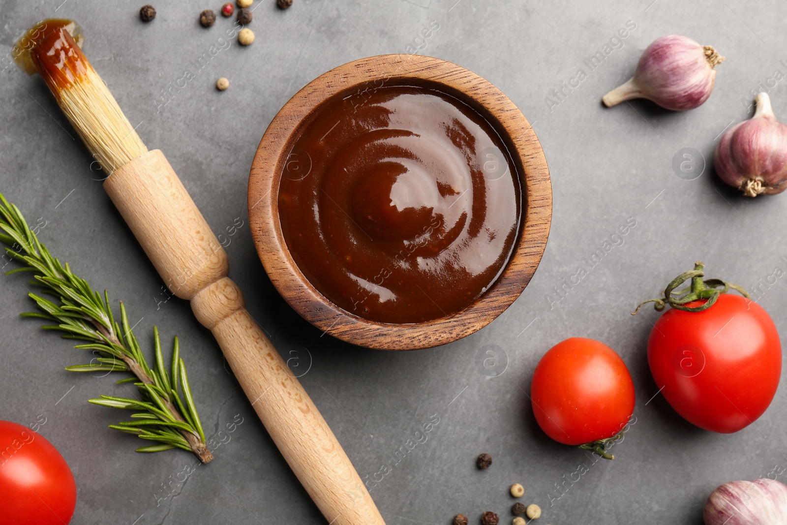 Photo of Flat lay composition with tasty barbeque sauce in bowl on grey textured table