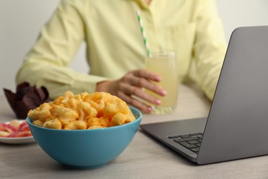 Bad habits. Woman eating different snacks while using laptop at wooden table, selective focus