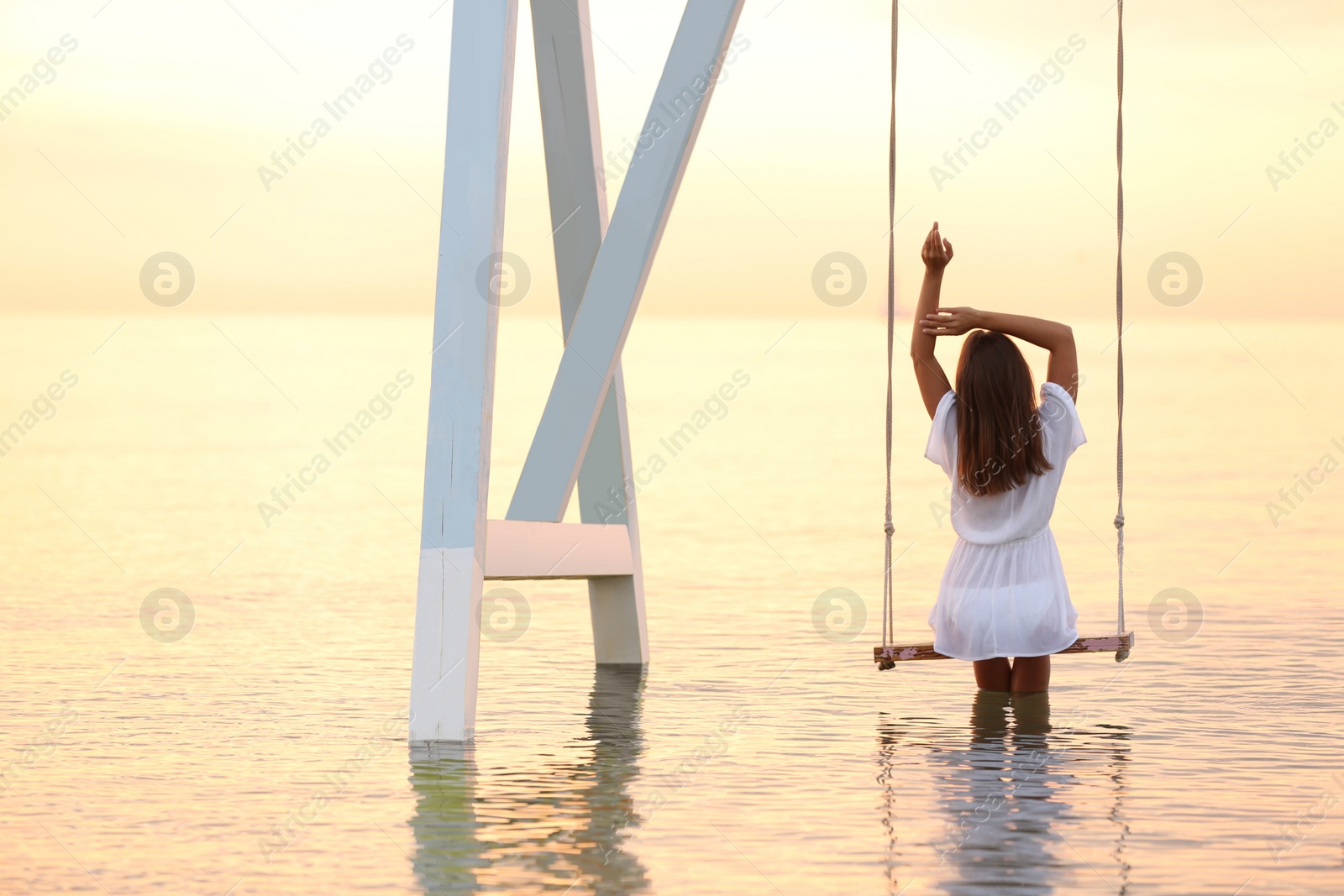 Photo of Young woman enjoying sunrise on swing over water