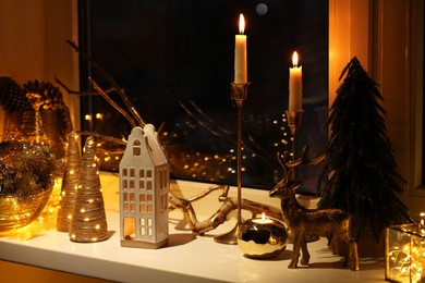 Many beautiful Christmas decorations, candlesticks and festive lights on window sill indoors