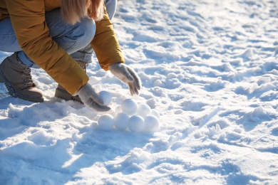 Woman rolling snowballs outdoors on winter day, closeup