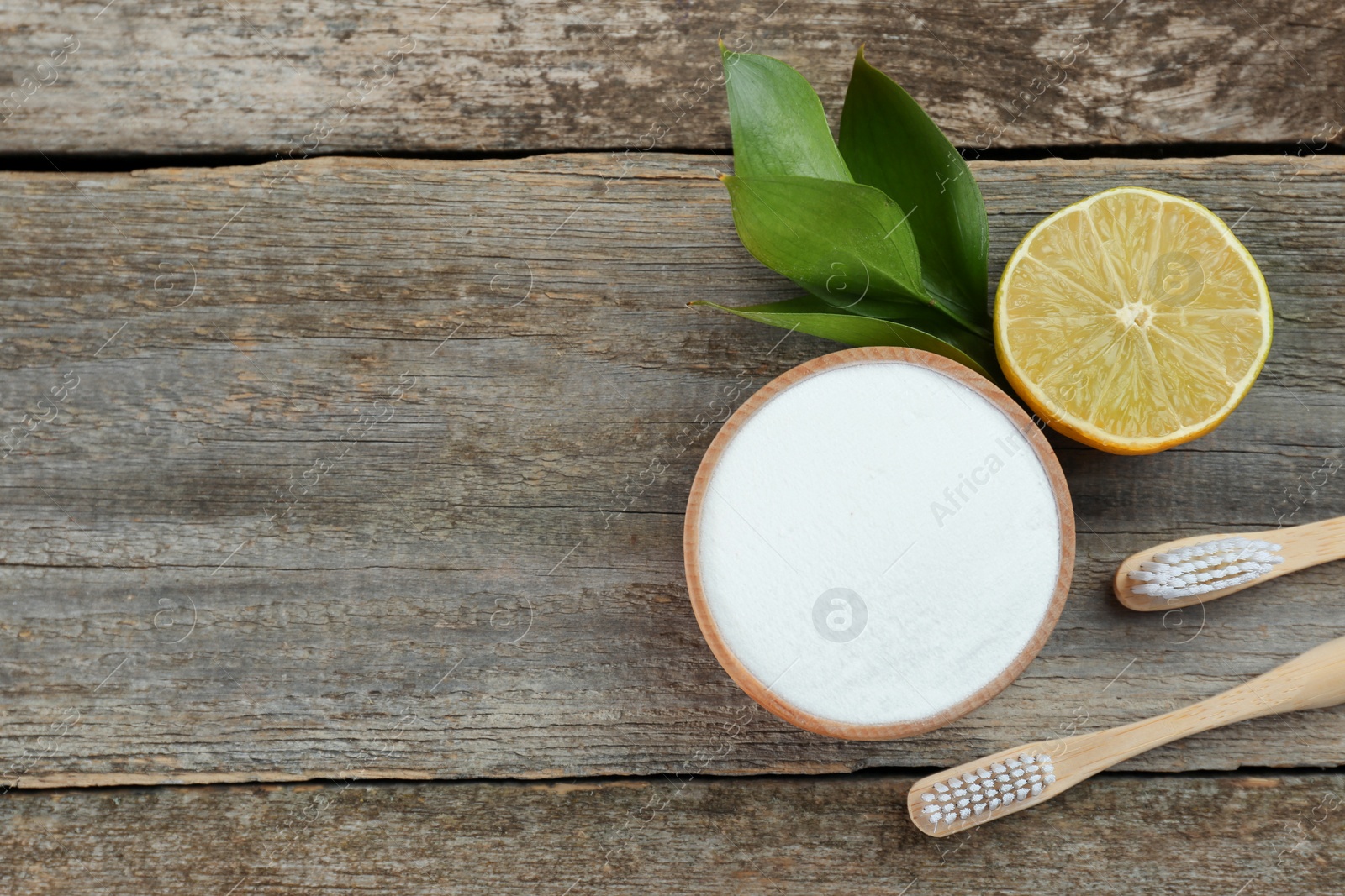 Photo of Bamboo toothbrushes, lemon and bowl of baking soda on wooden table, flat lay. Space for text